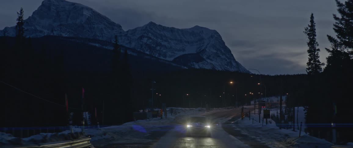 A vehicle driving on a bridge with a mountain range the sky and clouds in the background