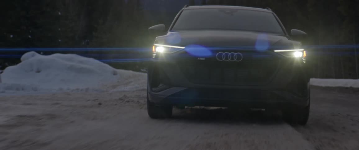 A black car travels on a snow covered road with headlights on