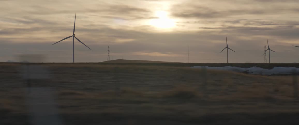 Wind turbines spin in a wind farm in a field on a cloudy evening