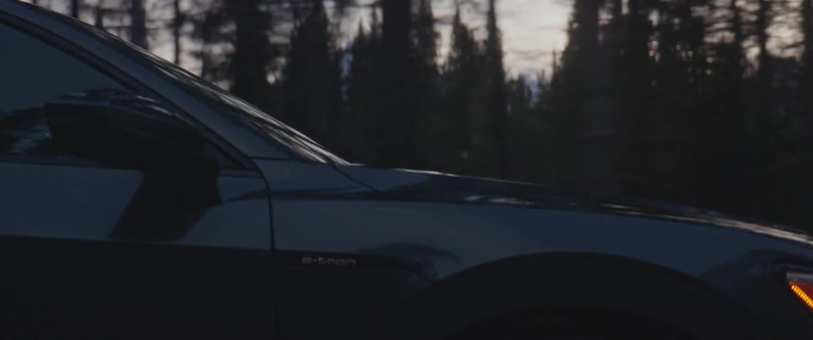 Dark grey audi car drives on snowy dirt road in the forest