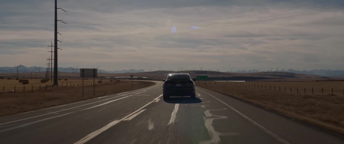 A vehicle travels a rural road with large fields surrounding