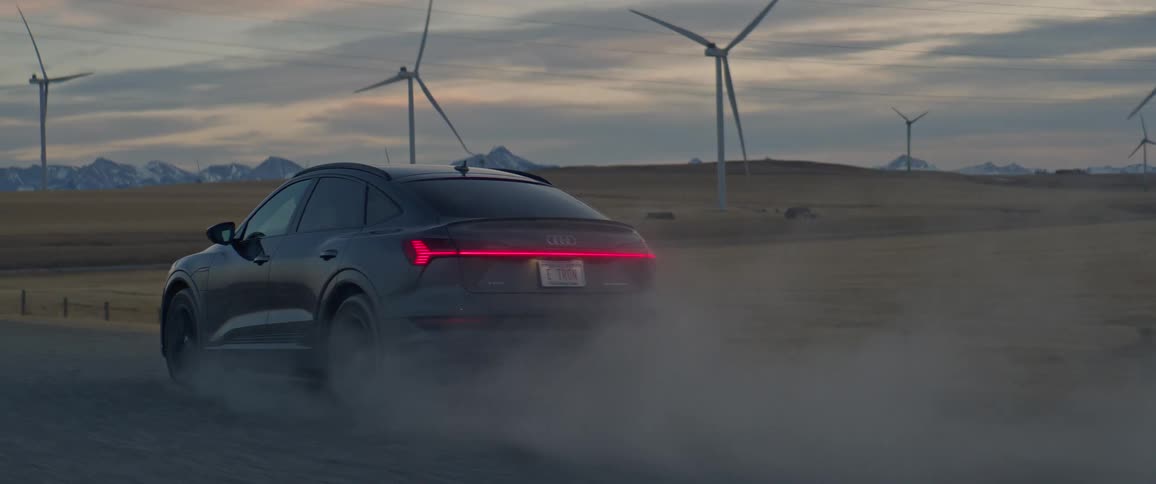 A black car travels on a road with spinning wind turbines along the roadside