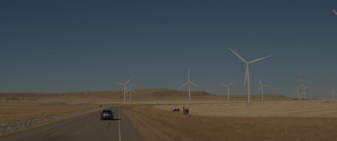 A vehicle driving on a road with wind turbines the sky and clouds in the background
