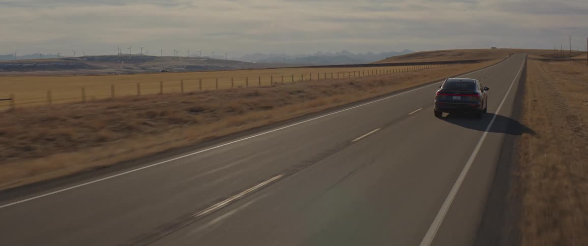 A vehicle driving on a road with wind turbines the sky and clouds in the background