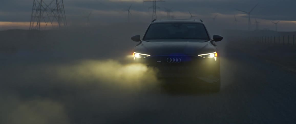 Headlights illuminate fog as car drives across plains near electric transmission tower at night