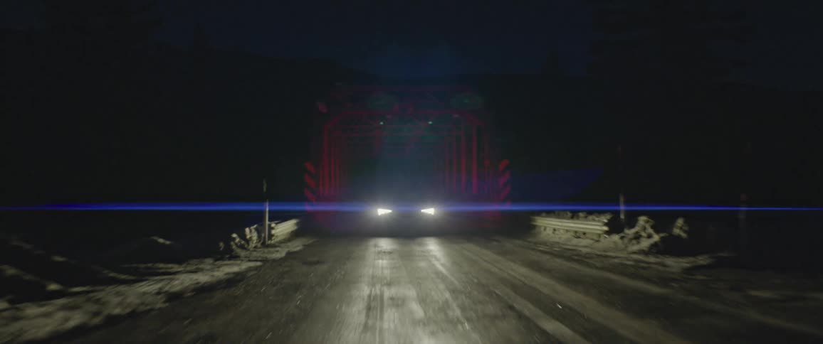 A car speeds along a remote road while its headlights pierce the darkness