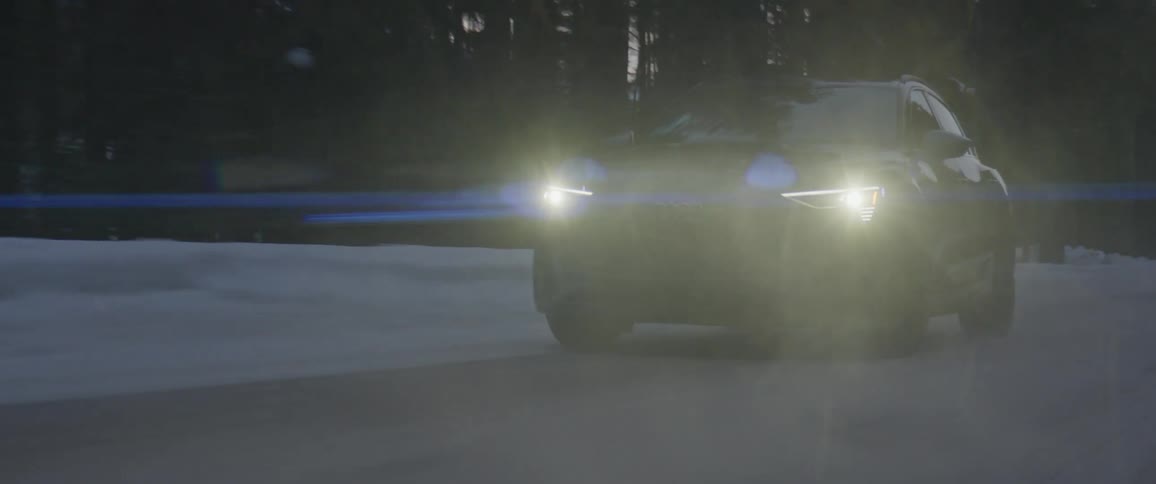 A vehicle travels along a road lined with snow through a forest in the evening