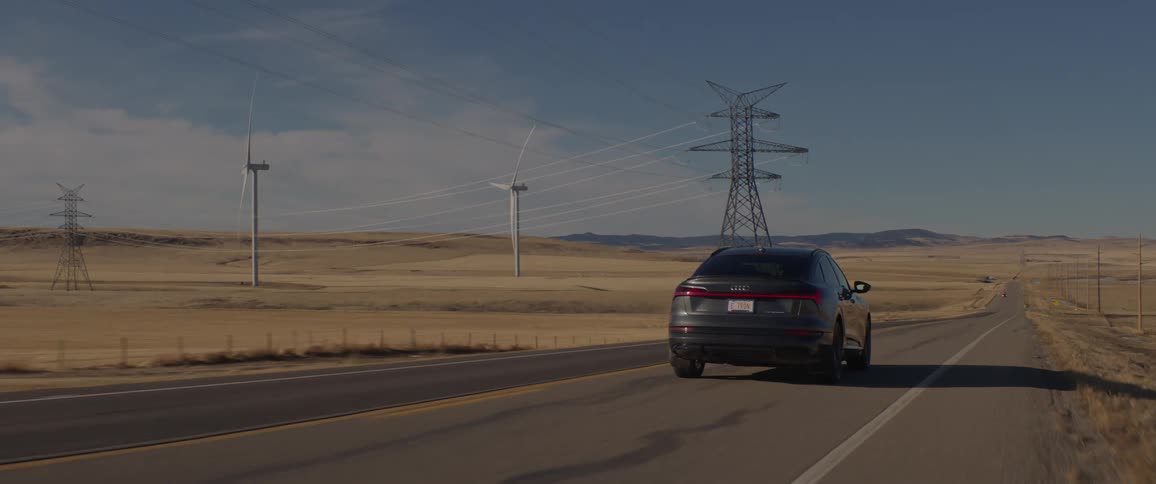 A vehicle driving on a road with wind turbines the sky and clouds in the background