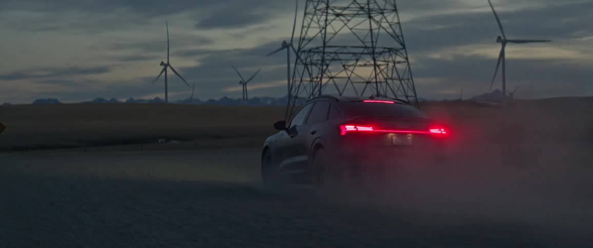 A vehicle drives on a dirt road beside wind turbines