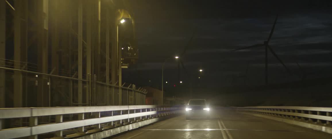 A vehicle driving on a road with wind turbines the sky and clouds in the background