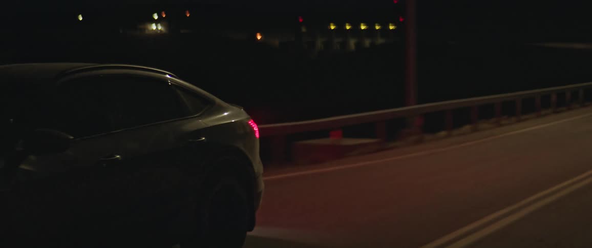 A single vehicle drives quickly along an empty road in the dark of night