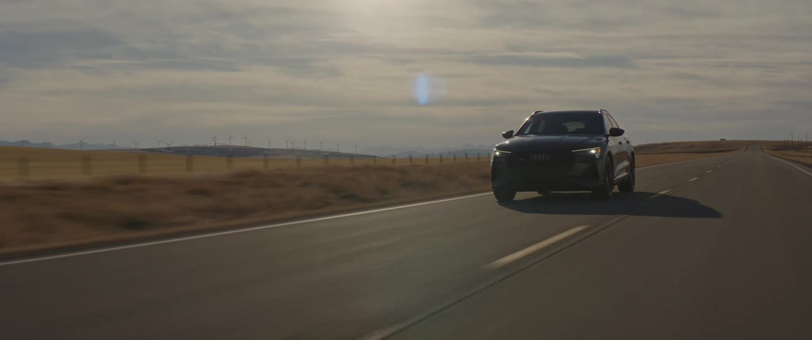 A vehicle driving on a road with a landscape the sky and clouds in the background