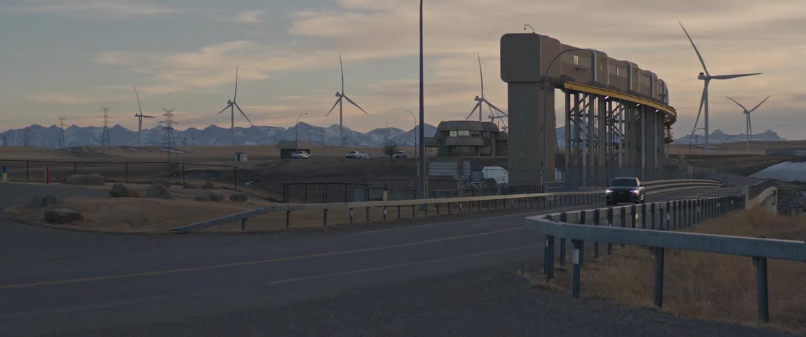 Black car driving over a bridge near a wind farm at morning