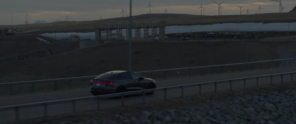 A black car travels on a road through a wind farm of spinning turbines