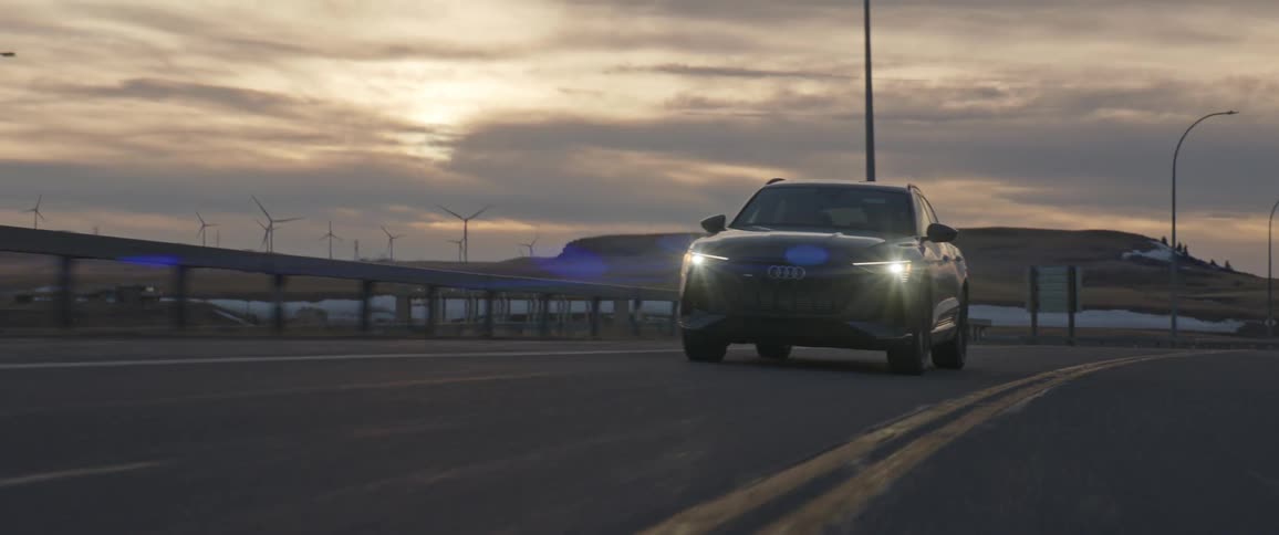 Car with headlights on driving on a road near the wind farm on the hills at sunset