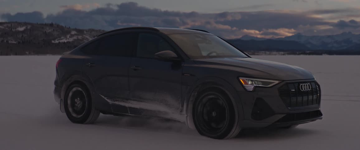Black car driving on a snow covered desert near the mountains at morning