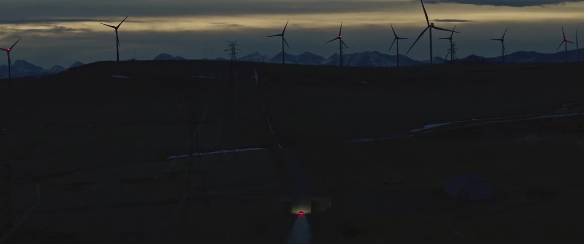 A car travels on a road near a wind farm of spinning wind turbines