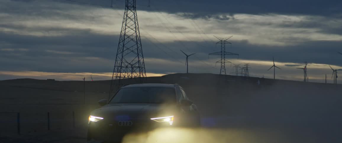 Black sports car with headlights on driving on a rural road next to transmission towers at evening