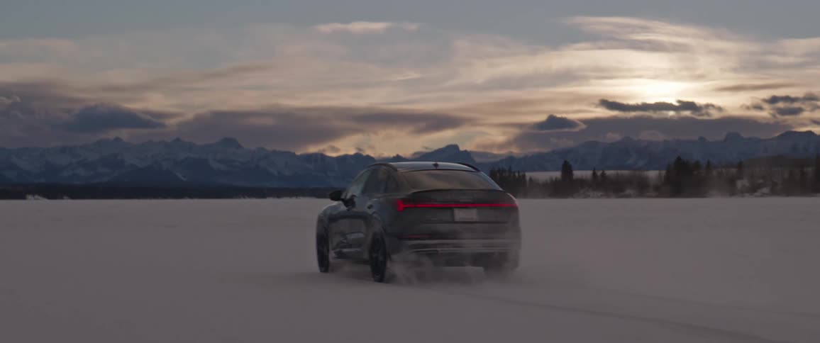 A black car travels through the snow as the sun is setting