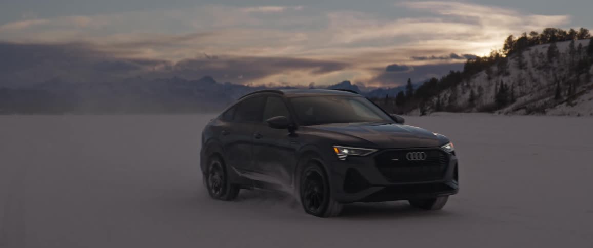 A vehicle driving in a snowy field with a mountain range the sky and clouds in the background