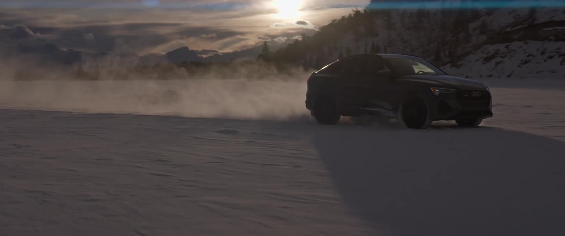 A vehicle driving in a snowy field with a mountain range the sky and clouds in the background