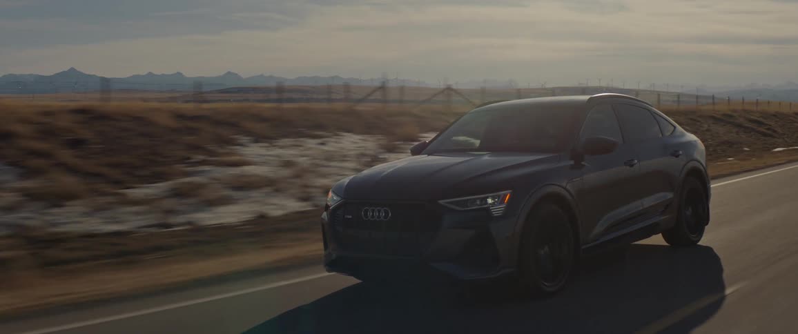 A black car travels on a two lane road on a cloudy day