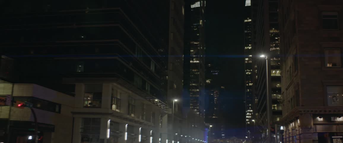 Vehicles with headlights driving on a city street with buildings and the sky in the background