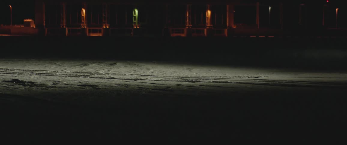 A vehicle driving on a snowy road with buildings and lights in the background