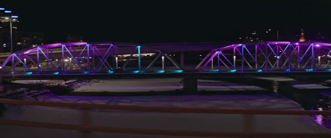 A purple illuminated bridge and high rise buildings seen from a moving vehicle