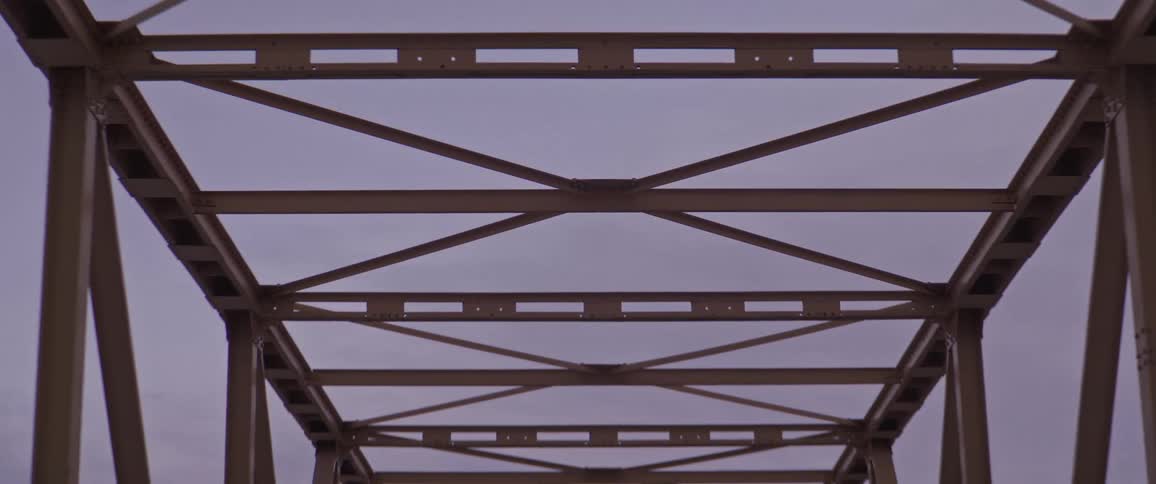 A vehicle driving on a bridge with a mountain range the sky and clouds in the background