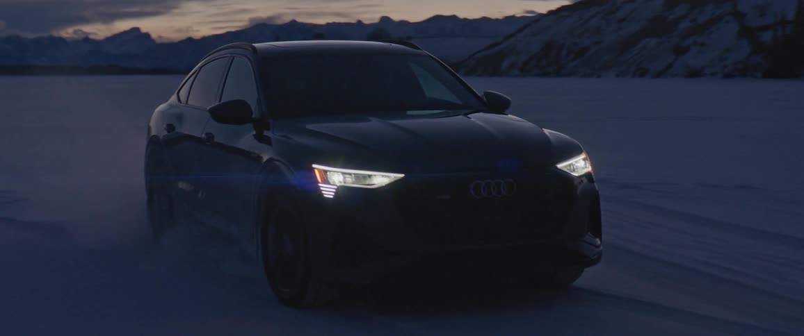 A vehicle driving on a snowy field with a mountain range the sky and clouds in the background