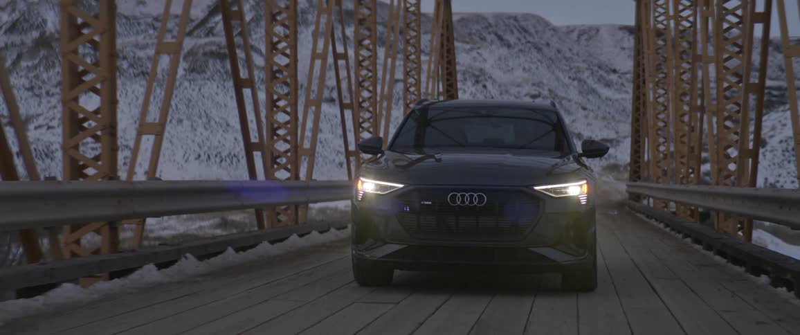 Black sports car driving over a bridge in the countryside near the mountains at morning