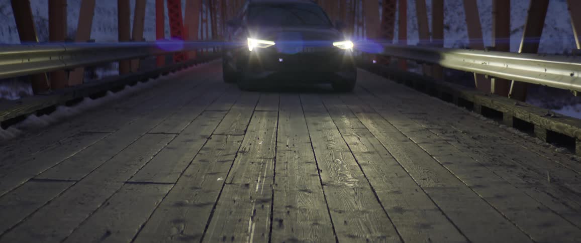 A black car with headlights on is sitting idle on a bridge