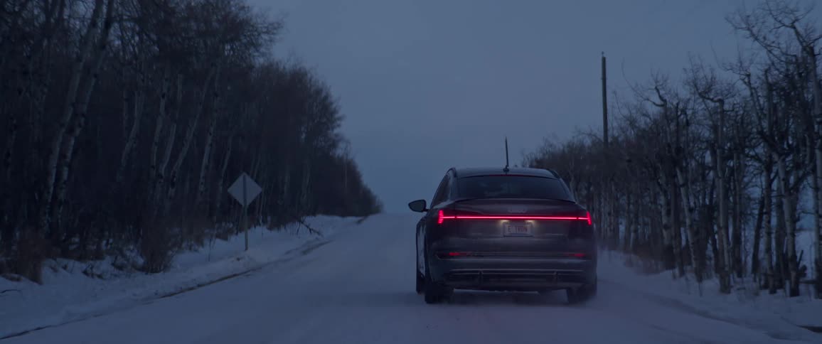 A black car pulls into a snow covered road and slides as it travels