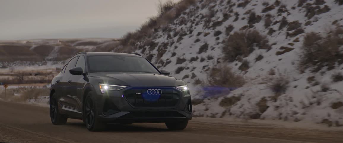 Black car drives along road winding through snow covered scrubby hills