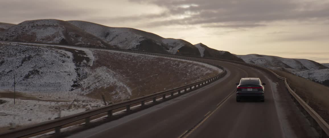 A vehicle driving on a road with a mountain range the sky and clouds in the background