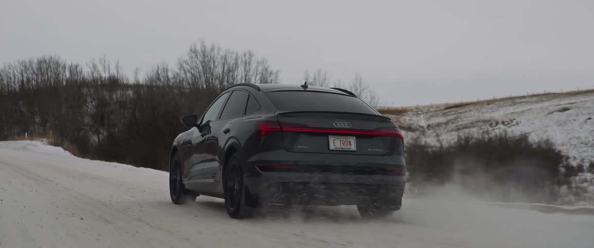 A vehicle driving on a snowy road with trees the sky and clouds in the background