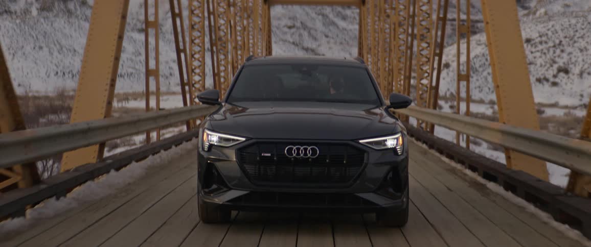 Black sports car driving over a bridge in the countryside near the mountains at morning