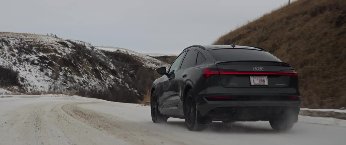 Black car driving on a snow covered road through the hills in the countryside at morning