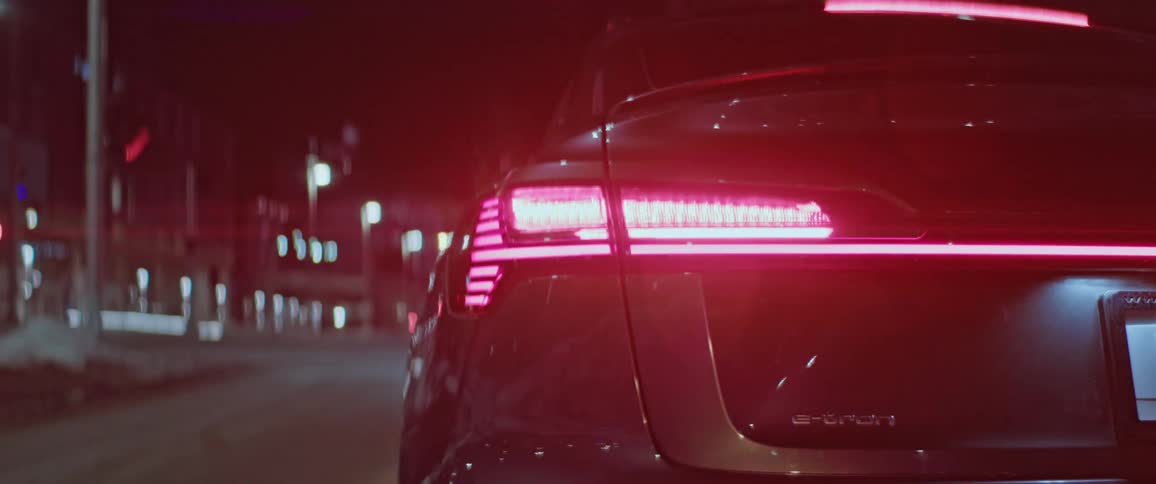 The tail light flashes on the back of a vehicle parked on the side of a road in a city at night