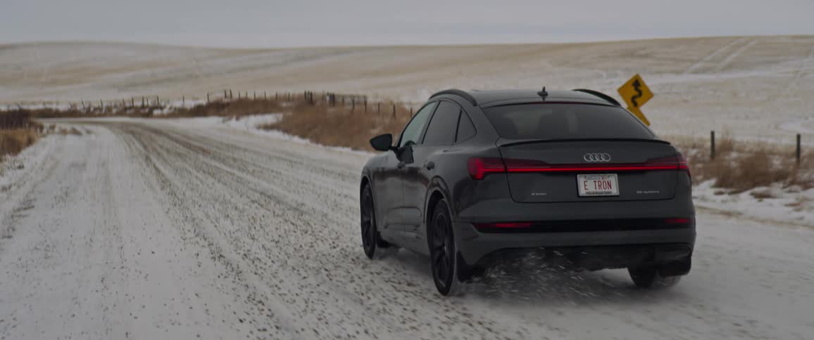 A vehicle driving on a snowy road with the sky and clouds in the background