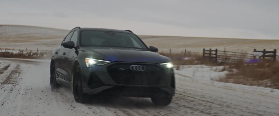 Dark gray audi car drives on snowy dirt road in the countryside