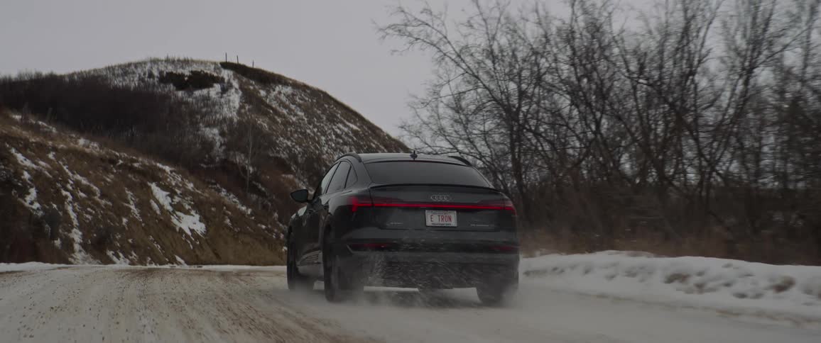A vehicle driving on a road with hills the sky and clouds in the background