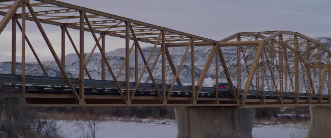 Black sports car driving over a bridge in the countryside near the mountains at morning