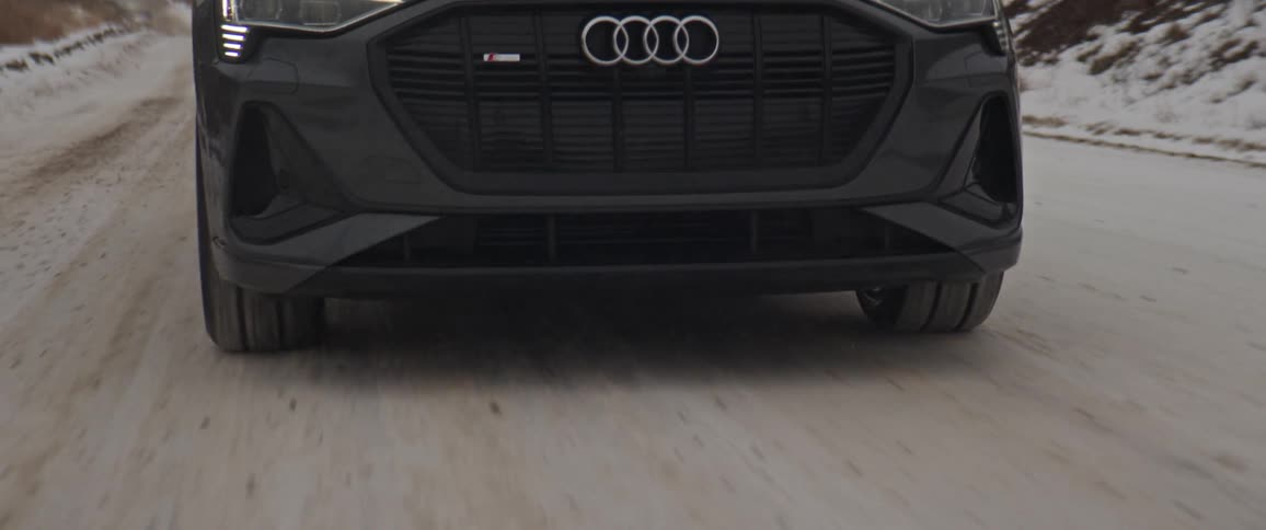 A black audi automobile travels on a snow covered mountain road