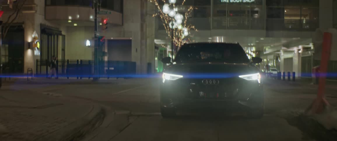 A black audi car is driving on a city street with multiple show rooms visible in background