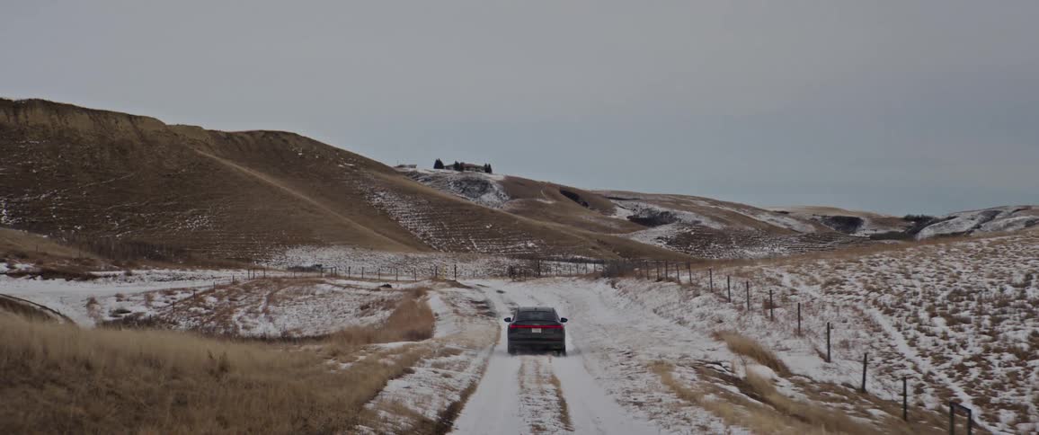 Dark grey audi car drives on snowy dirt road with hills in the background