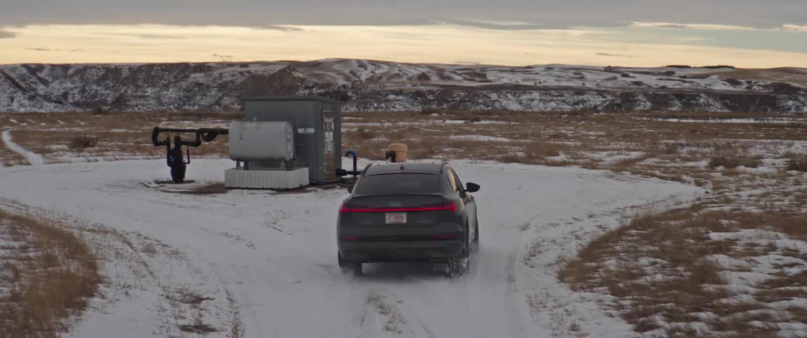 Black car circling a pumping station on a snow covered field in the countryside at morning