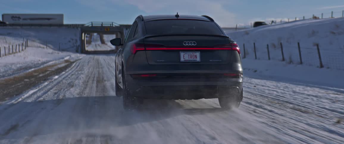 A vehicle driving on a snowy road with an overpass the sky and clouds in the background