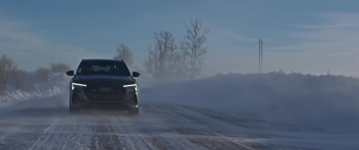Dark gray audi car drives snowy downhill in the field